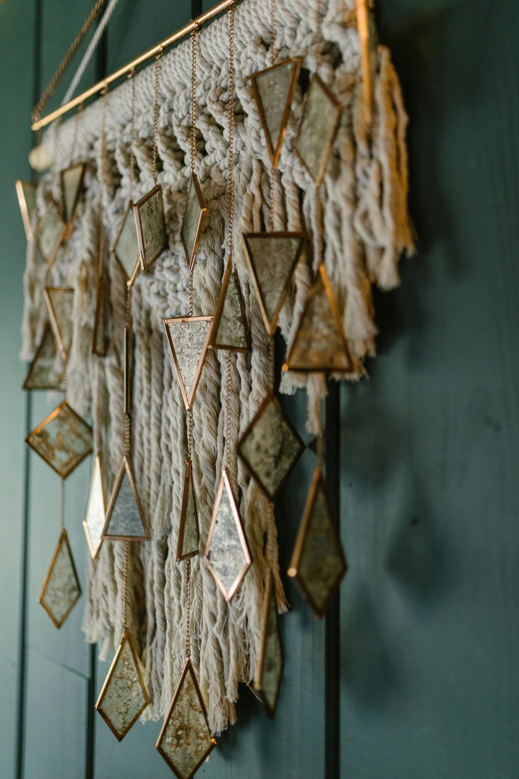 Detailed macrame wall hanging with geometric mirror accents on a green background.