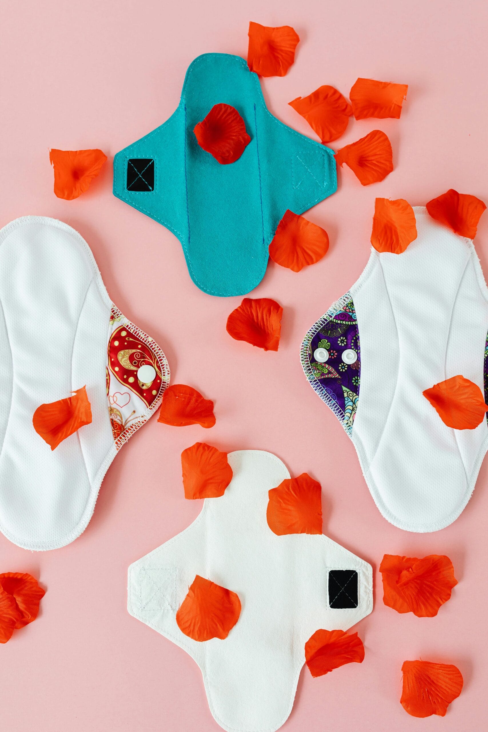 Reusable cloth menstrual pads with red petals on a pink background promoting sustainable menstrual products.